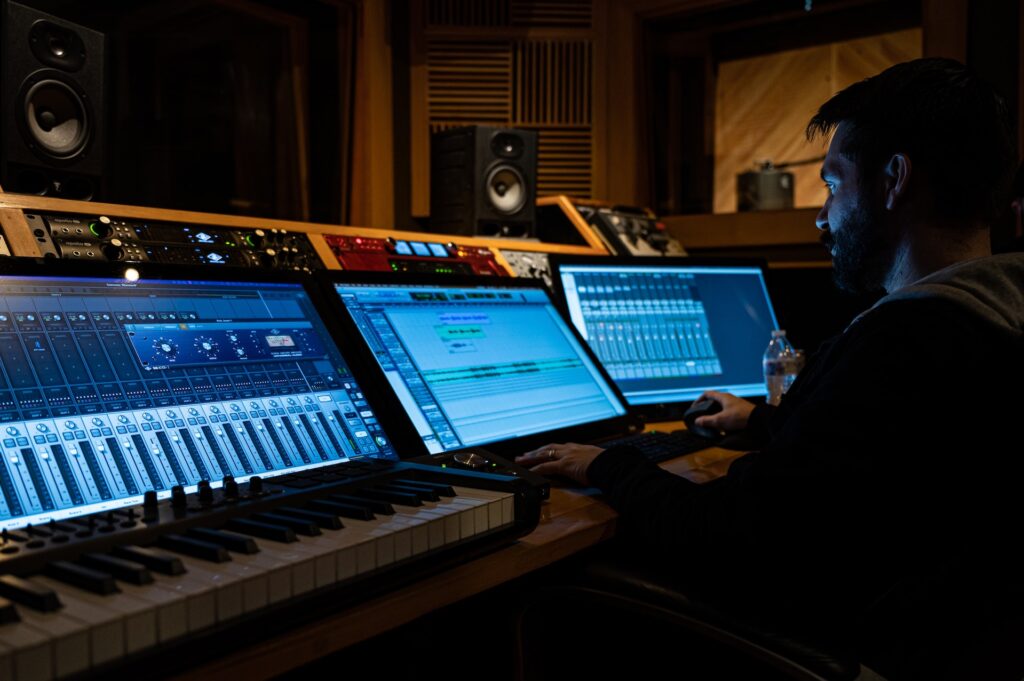 An audio engineer is sitting in front of the mixing console in the professional studio 